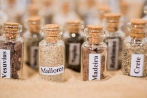 Numerous small apothecary bottles lie on the sand, with different sand contents, labeled with places such as Madeira and Mallorca.