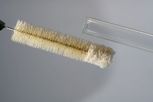 From the right into the picture held the upper part of a test tube, from the left a test tube brush, in front of gray background